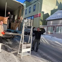 Mannskaper bærer møbler ut av en container en vinterdag