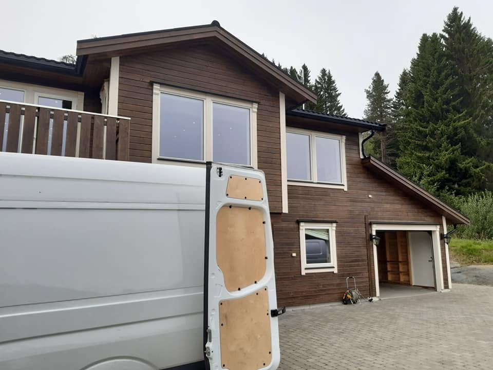 Hvit flyttebil med åpen bakdør utenfor trehus i skogkanten